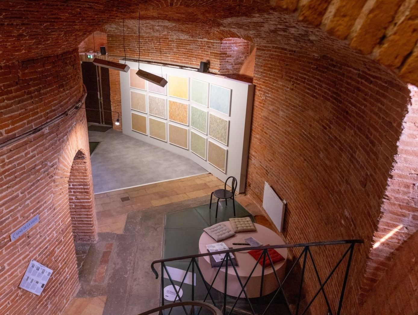 Vue de l'exposition de Laurent Lafolie depuis l'escalier menant au sous-sol avec poufs pour s'asseoir